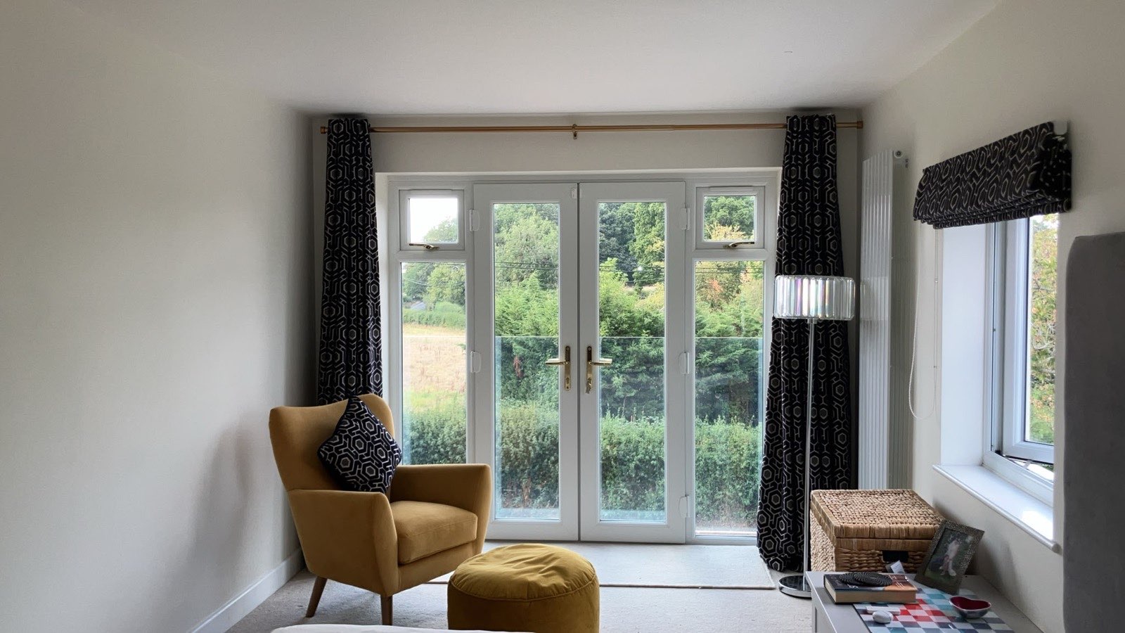 Bedroom with full-length patterned curtains at the French doors and a roman blind in the same fabric at the smaller window to the right