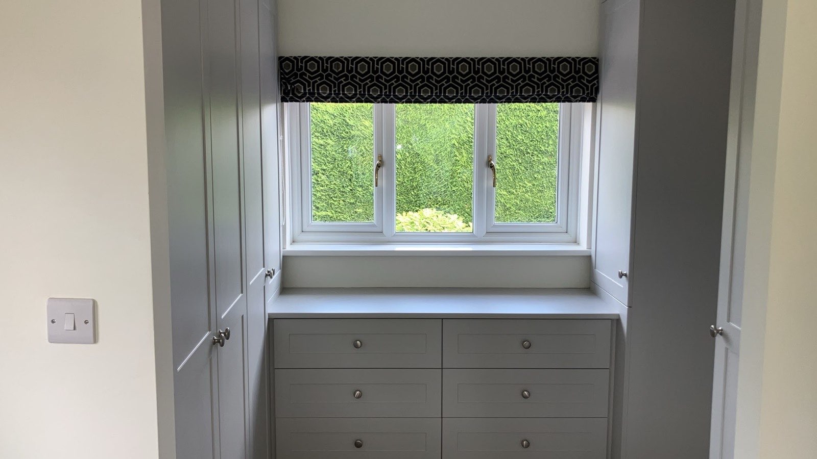 The dressing room window with a roman blind in the same patterned cut velvet, above fitted drawers and between painted wardrobes